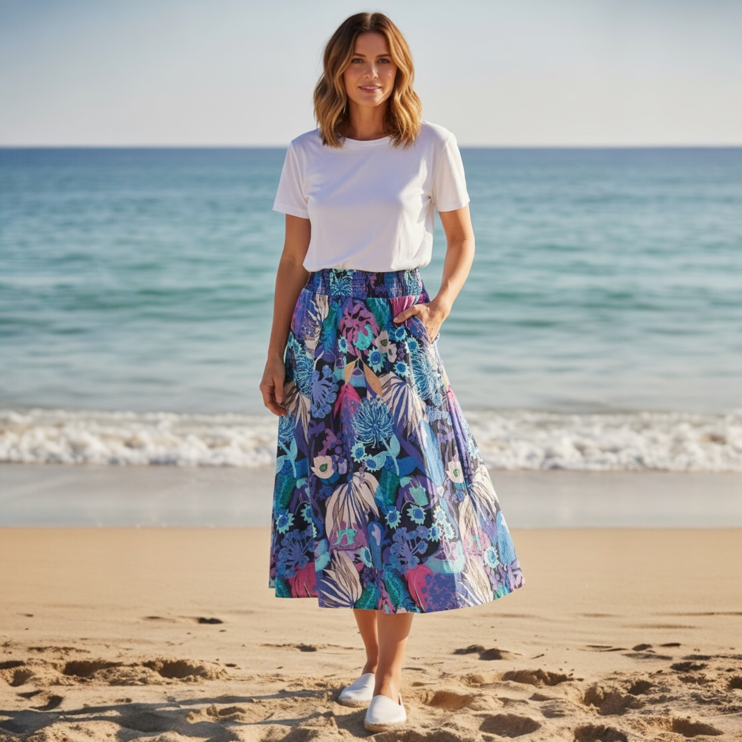 Woman standing on a beach wearing a colourful floral skirt with original artwork on sustainable fabric