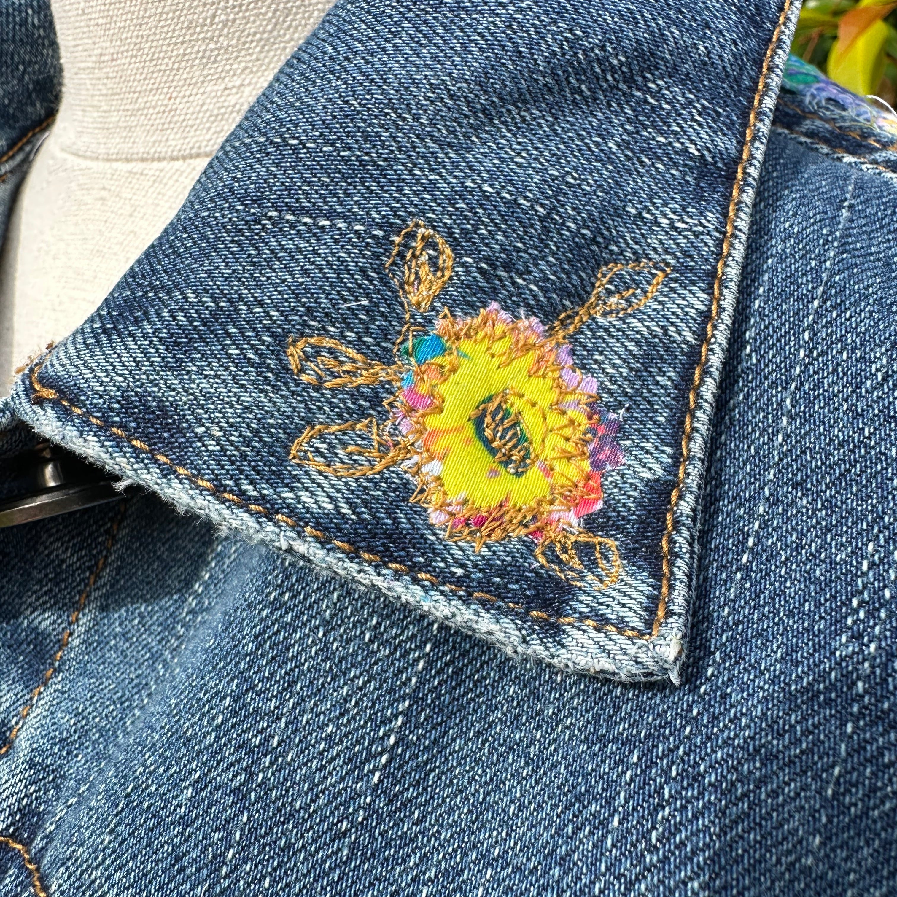 Bold recycled denim jacket transformed into vibrant wearable art, part of sustainable women's fashion.collar