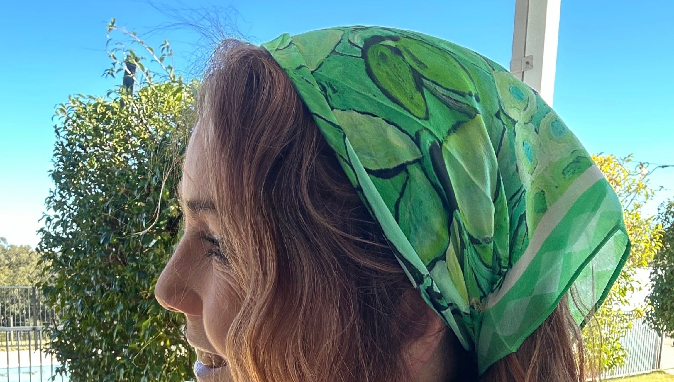 Green botanical wearable art bandanna with vibrant floral-inspired artwork worn as a stylish women’s headscarf and boho hair accessory