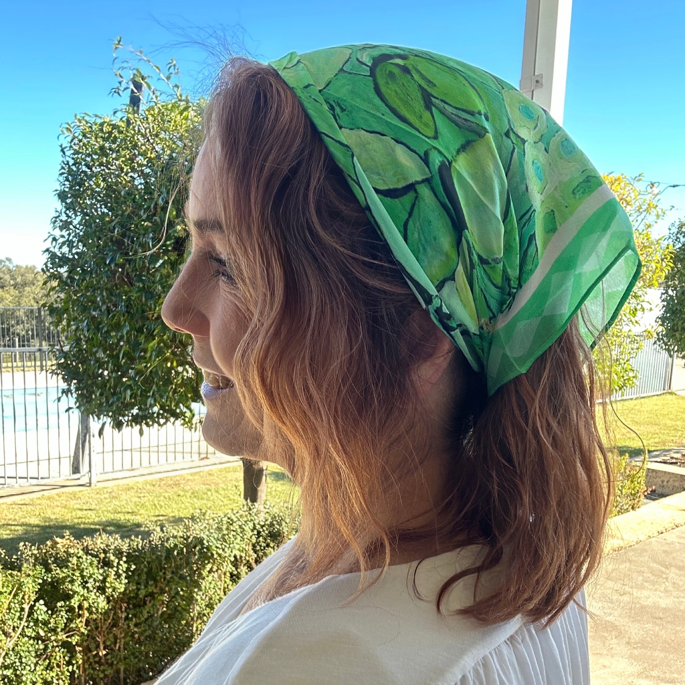 Green botanical wearable art bandanna with vibrant floral-inspired artwork worn as a stylish women’s headscarf and boho hair accessory